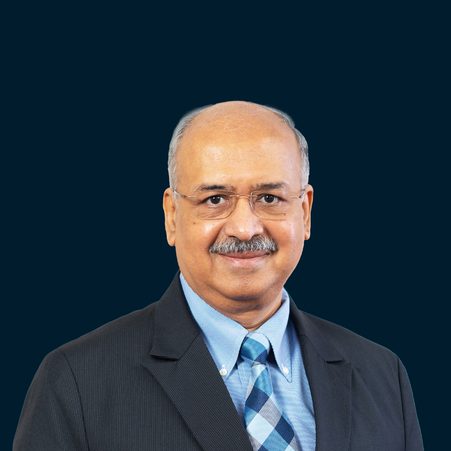Formal portrait of Dilip Shanghvi in a dark suit and light blue shirt against a deep navy background.