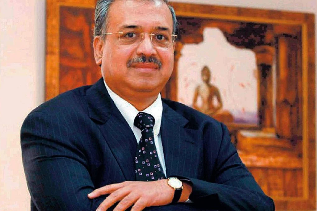 Dilip Shanghvi seated in a dark suit in an office, with a framed artwork behind him.