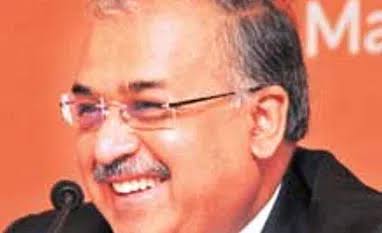 Dilip Shanghvi smiling at a press event, photographed against an orange backdrop.
