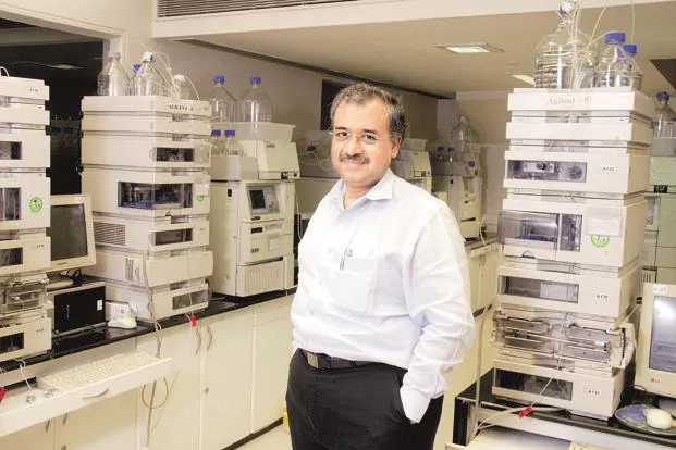 Dilip Shanghvi standing in a laboratory surrounded by analytical chromatography instruments.