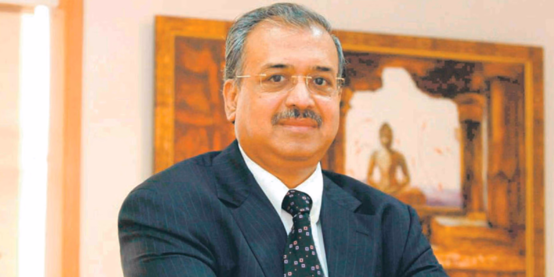 Dilip Shanghvi seated in a dark suit in his office, with a framed artwork behind him.