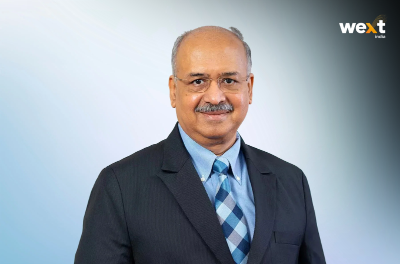 Dilip Shanghvi in a dark suit and blue checked tie, photographed against a graduated blue background.