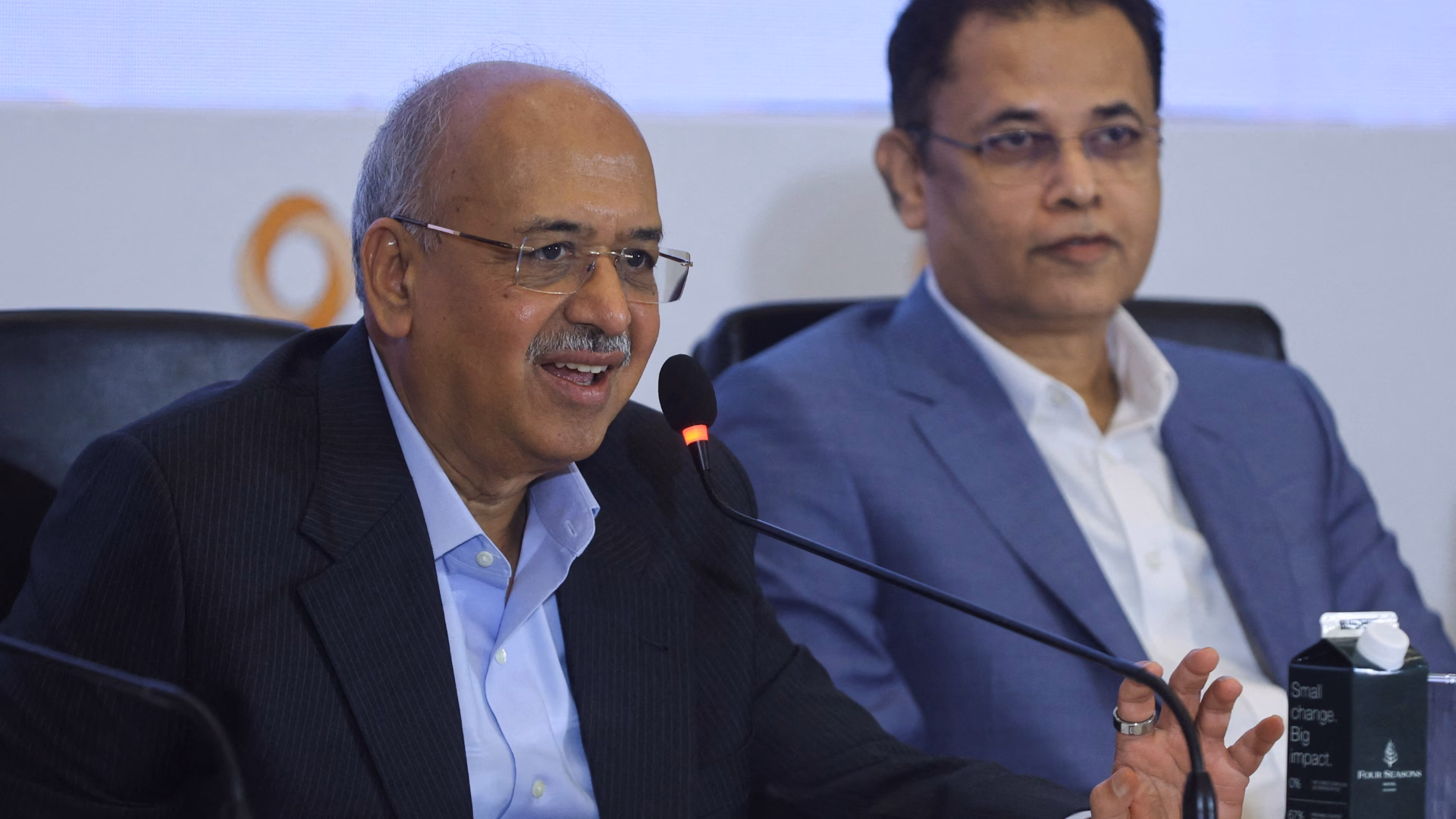 Dilip Shanghvi speaking into a microphone at a company press conference alongside a colleague.