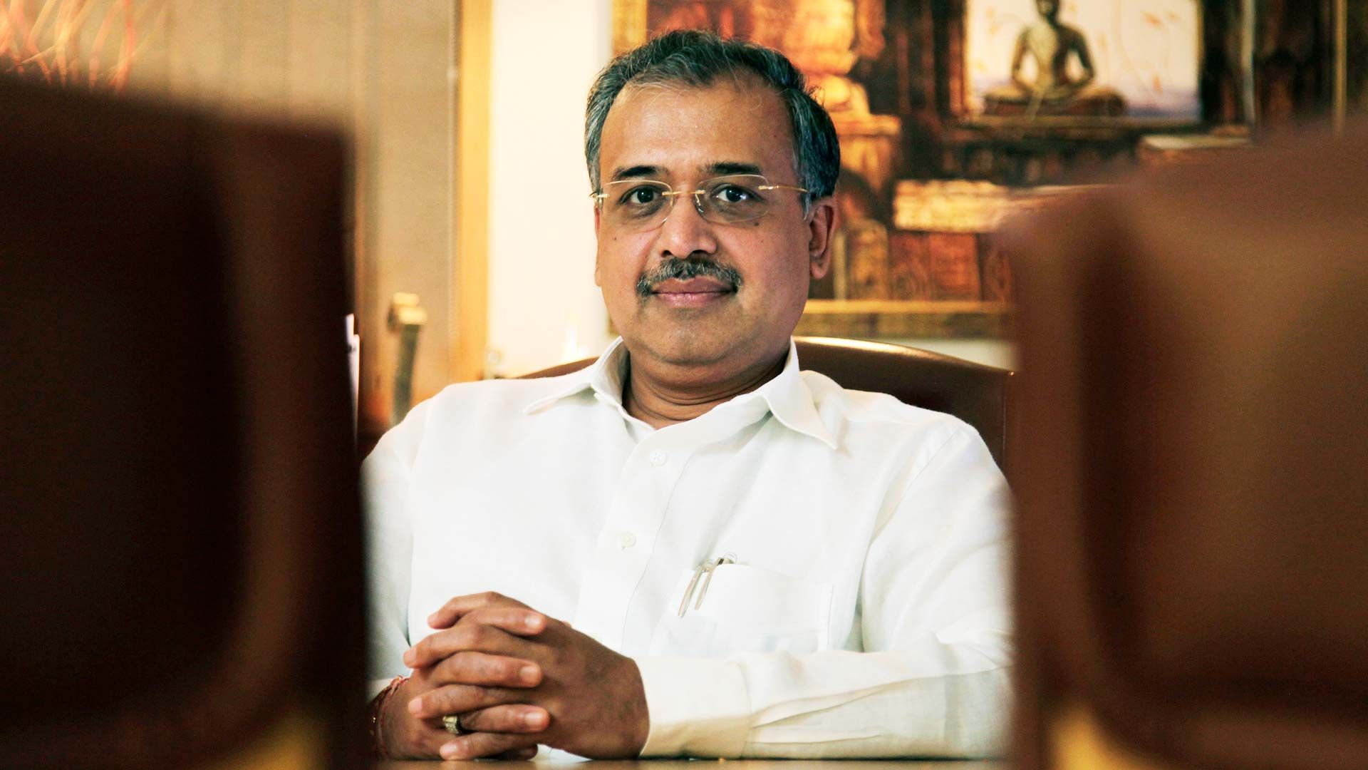 Dilip Shanghvi seated at his desk with hands folded, in a white kurta.