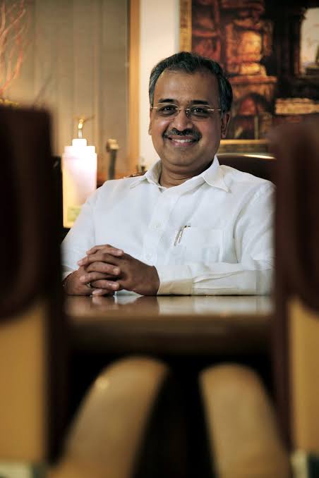 Portrait of Dilip Shanghvi, founder of Sun Pharmaceutical Industries, seated at a table in a white shirt.
