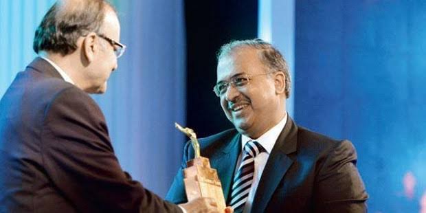 Dilip Shanghvi receiving an award trophy on stage, shaking hands with the presenter.