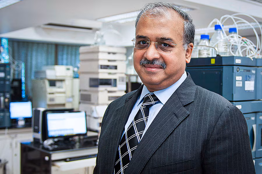 Dilip Shanghvi photographed in a Sun Pharma analytical laboratory beside chromatography instruments.